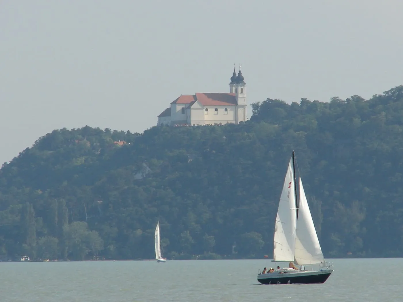Tihany Abbey on its wooded hill above Lake Balaton, with a sailing boat on the water