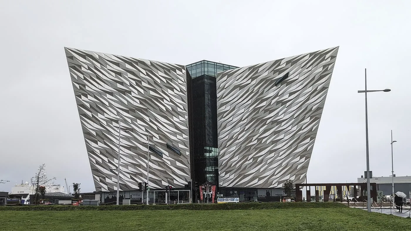 The angular silver-clad hull-shaped wings of Titanic Belfast with a glass and dark-glazed centre, under a grey sky