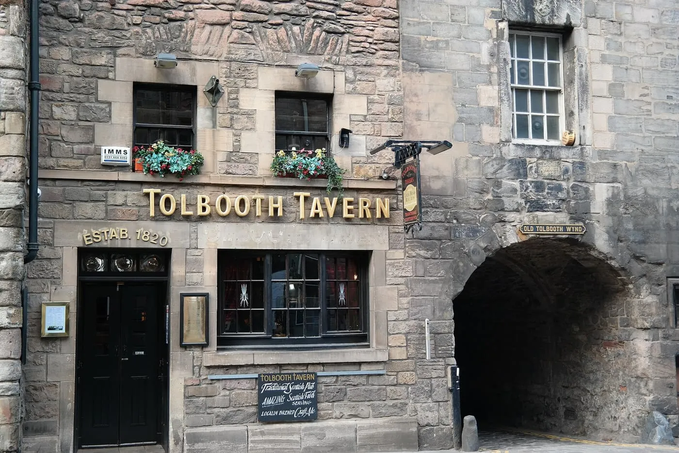 The stone front of the Tolbooth Tavern on the Royal Mile, with its gold lettering, window boxes and an arched close beside it