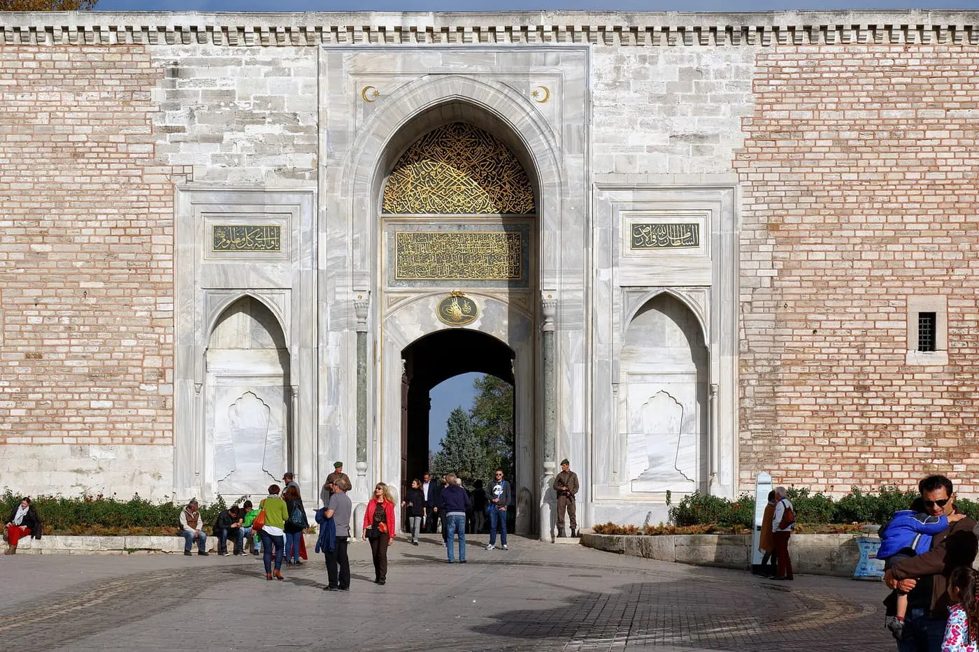 The Imperial Gate of Topkapı Palace, a tall pointed marble arch in a pale brick wall, with visitors at its foot