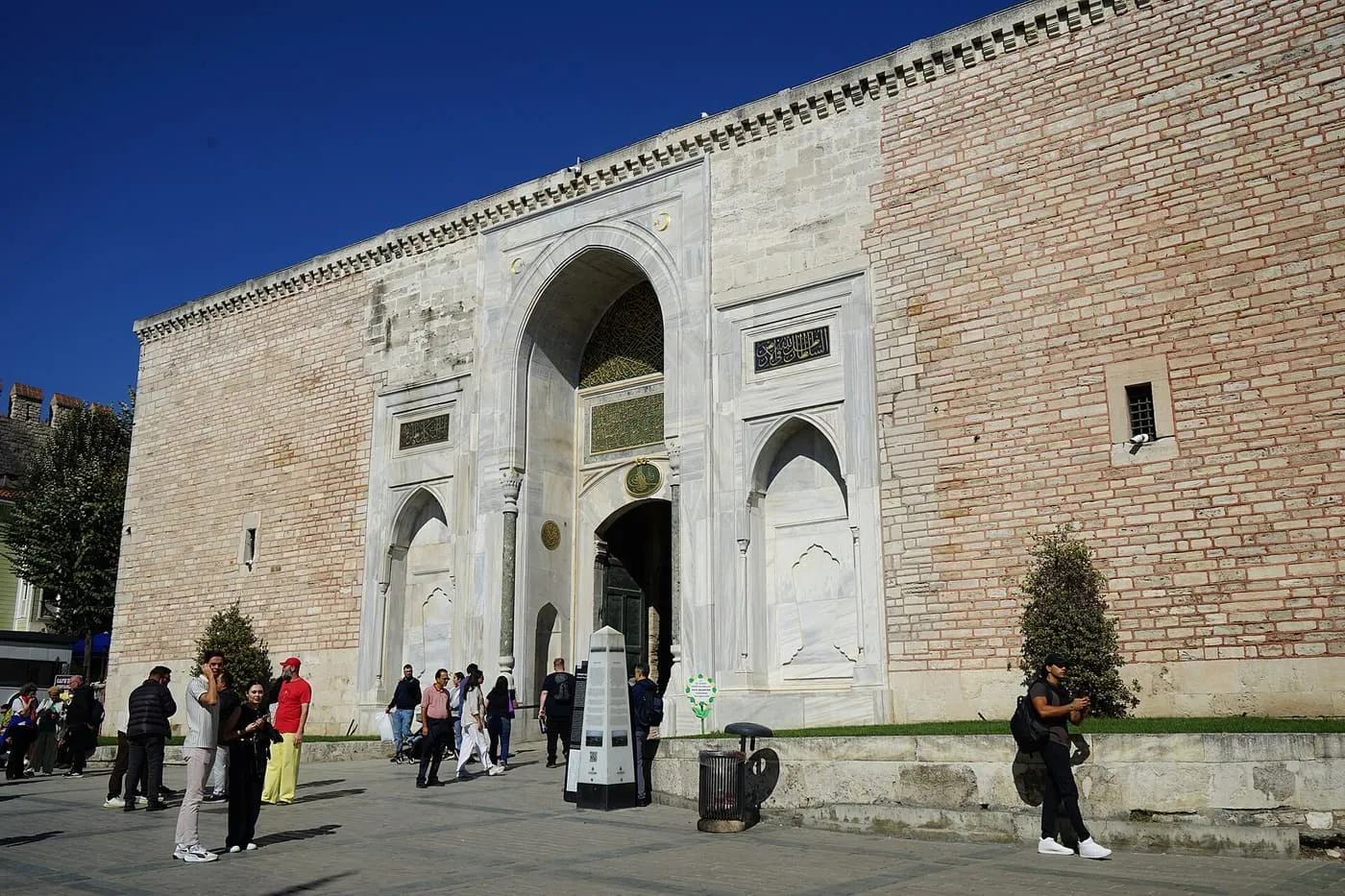 The marble-framed Imperial Gate in the high brick wall of Topkapı Palace, with visitors crossing the square in front