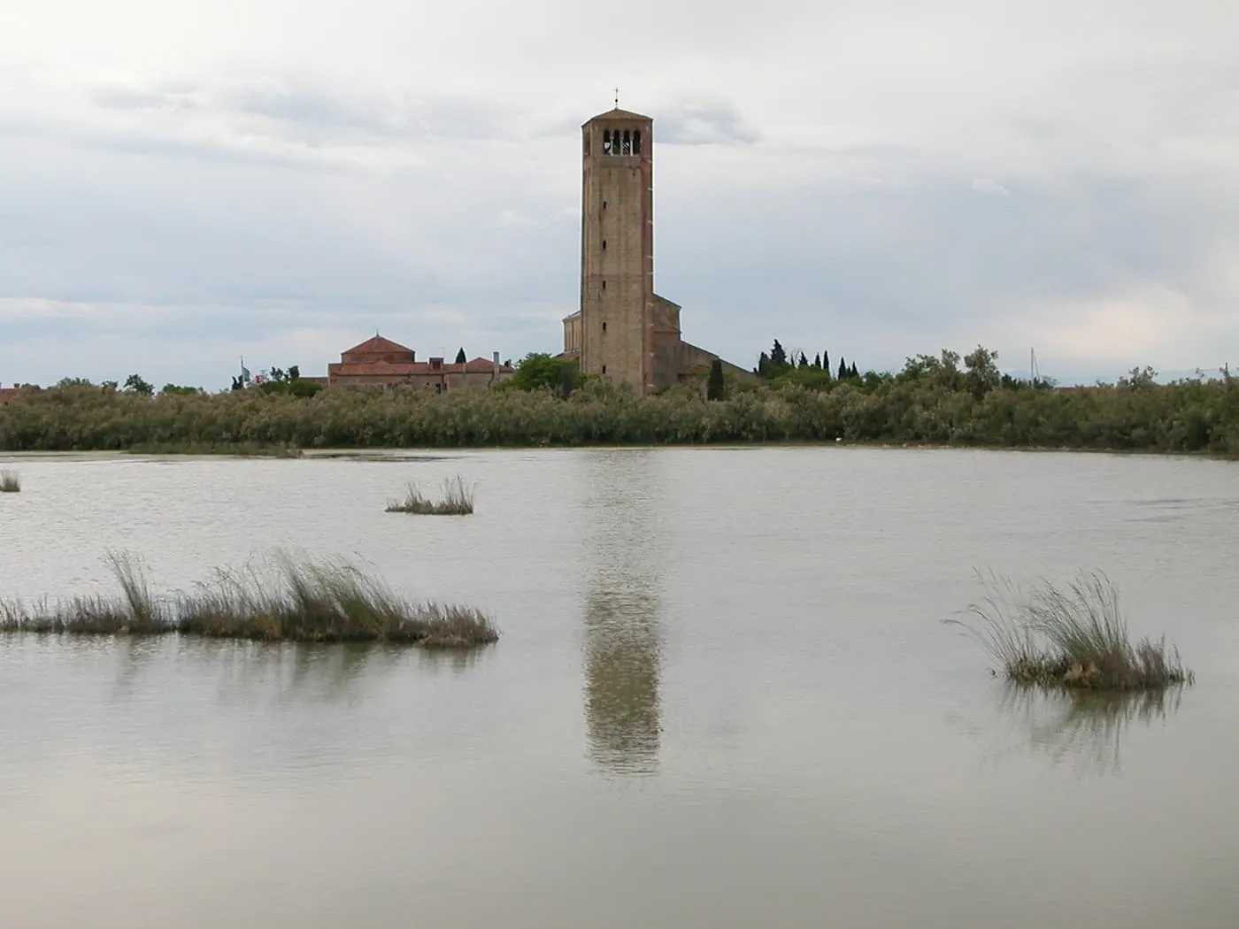 A tall brick campanile rising above reeds and a lagoon marsh