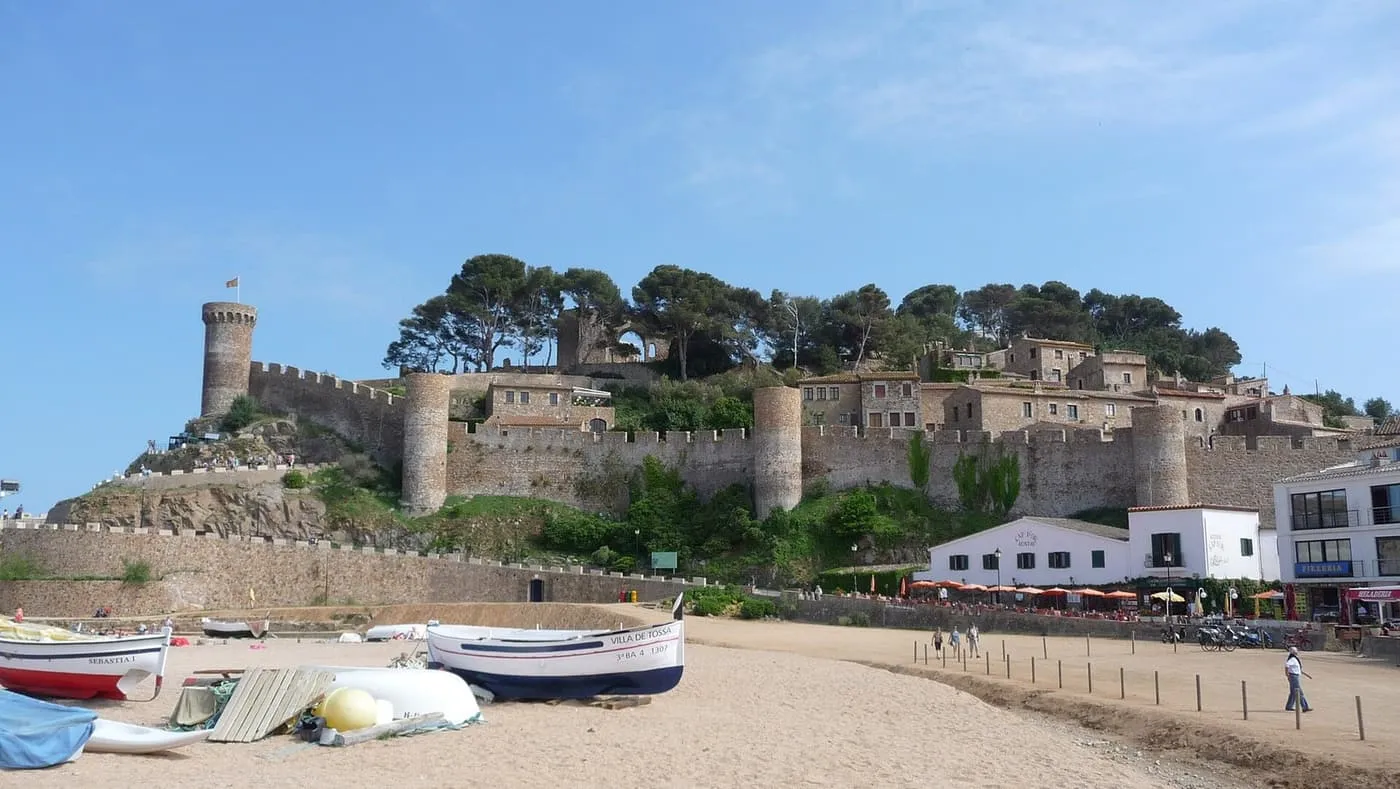 The walls and round towers of Tossa de Mar's Vila Vella above the beach, with fishing boats drawn up on the sand