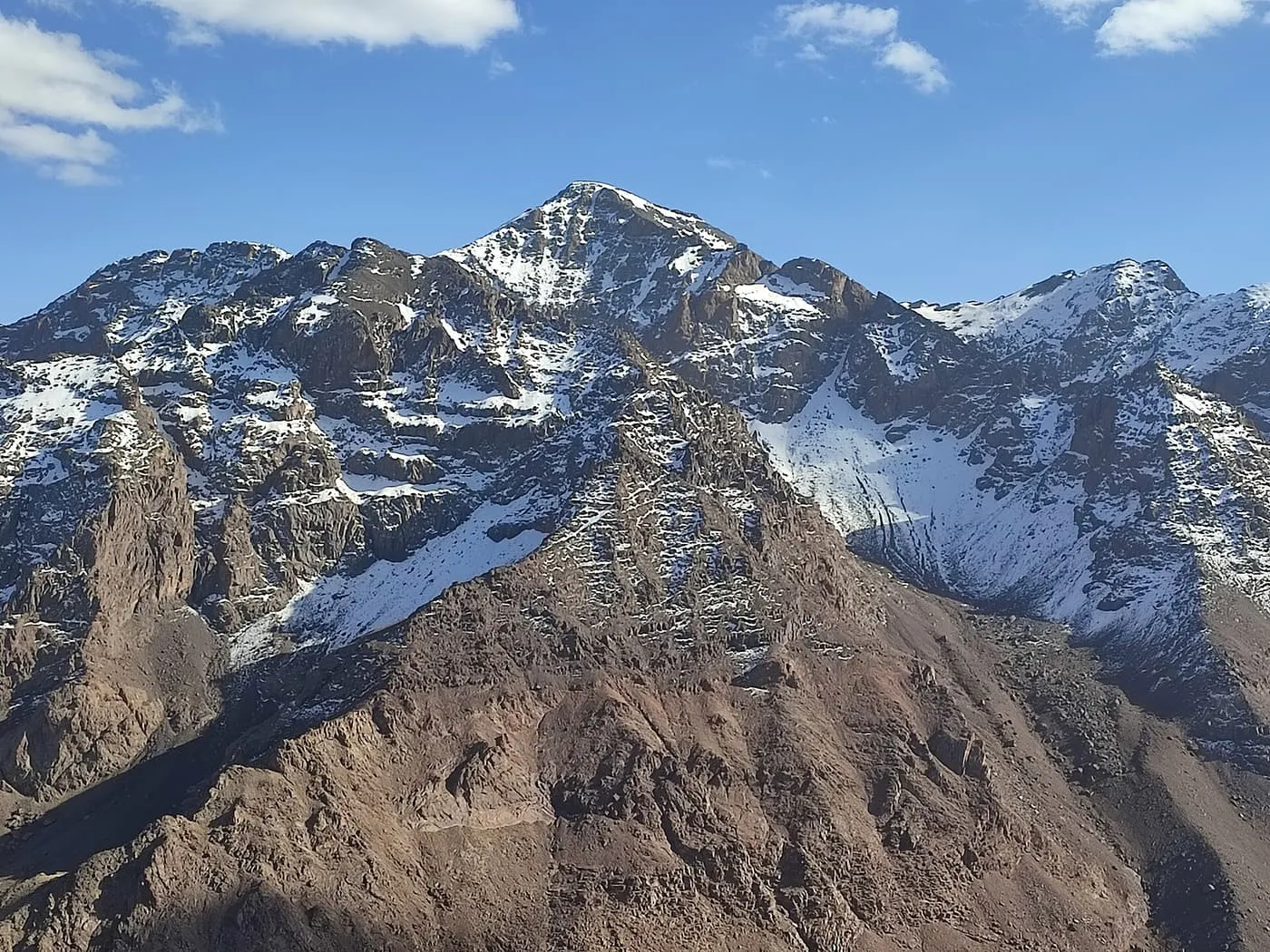The snow-streaked rocky summit of Jbel Toubkal against a blue sky