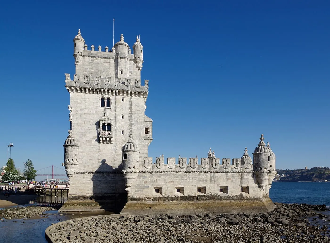Belém Tower, a pale limestone tower with turrets and a battlemented bastion, beside the Tagus under a blue sky