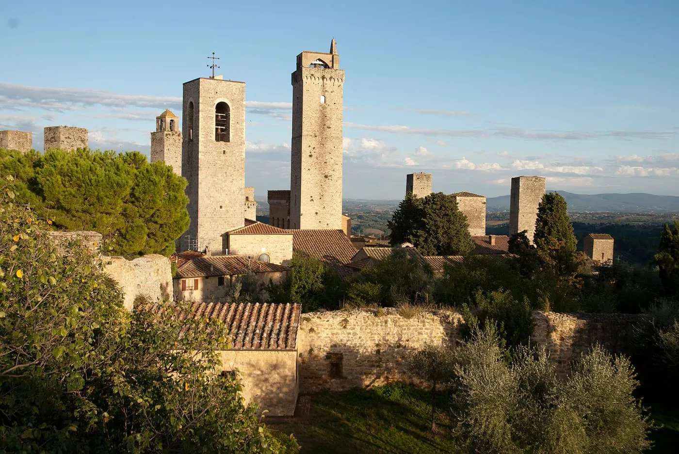 Medieval stone towers rising above olive trees and tiled roofs in San Gimignano