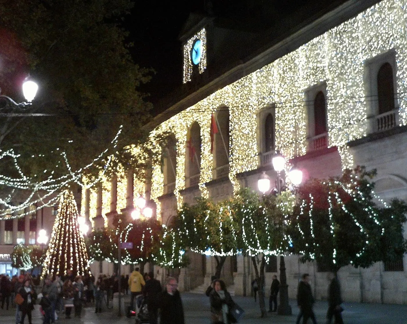 Seville's Town Hall with its stone façade covered in white lights, a lit tree beside it and crowds in the square