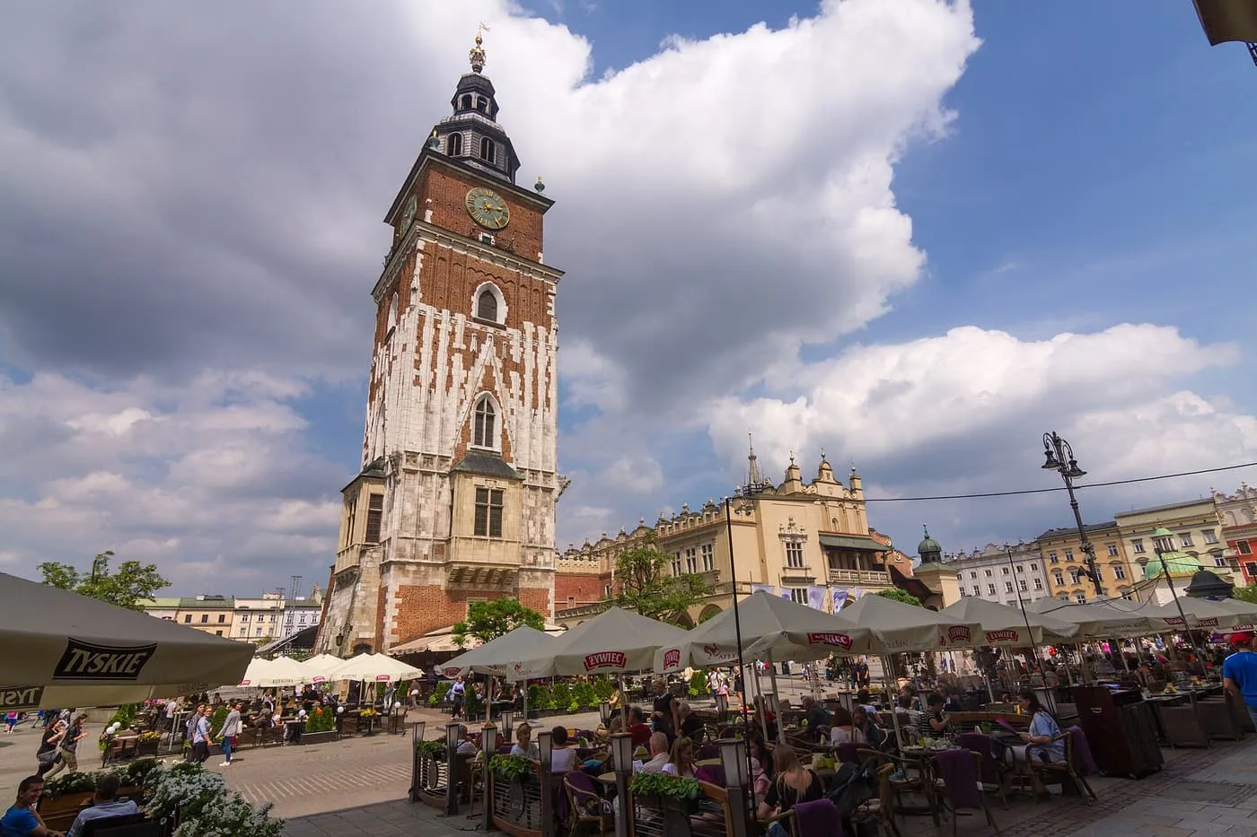 The Town Hall Tower, a tall brick and stone tower with a clock and a dark Baroque spire, above café tables on the square