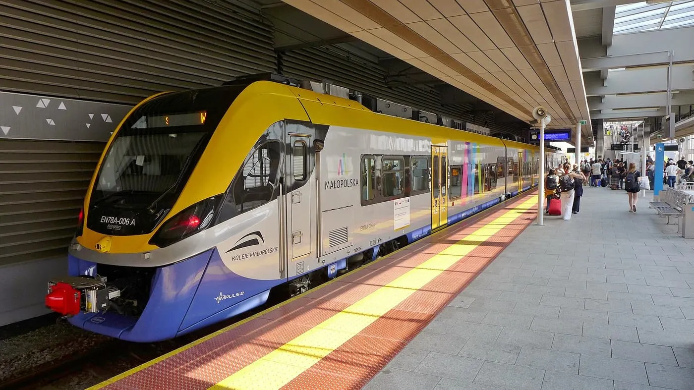 A yellow, grey and blue Koleje Małopolskie train at a covered platform at Kraków Lotnisko station