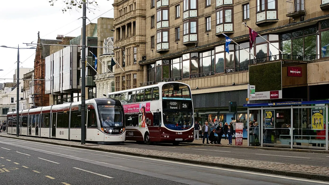 An Edinburgh tram and a maroon Lothian double-decker bus beside the Princes Street tram stop