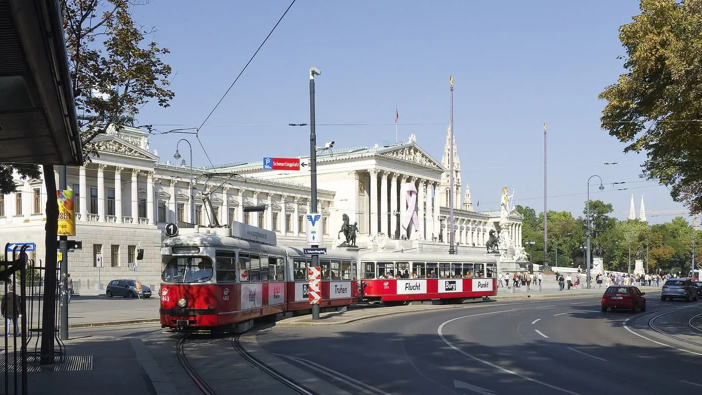 A red-and-white tram on line 1 rounding the bend of the Ringstrasse in front of the columned Parliament building