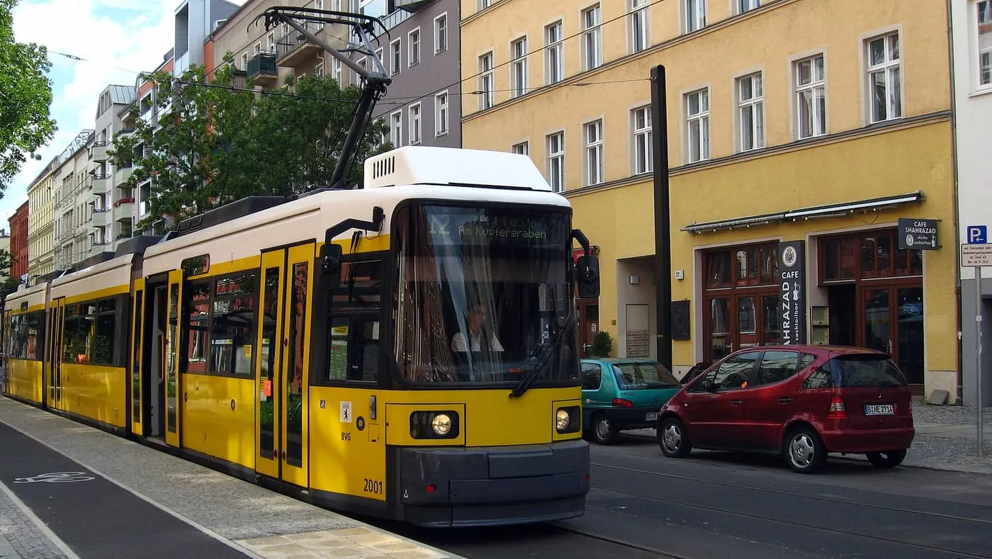 A yellow BVG tram stopped at the kerb on Pappelallee, with apartment buildings behind