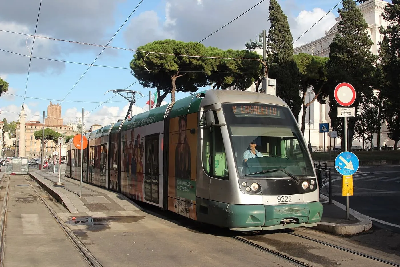 An ATAC tram at a stop by Piazza Venezia, with pine trees and the Vittoriano behind