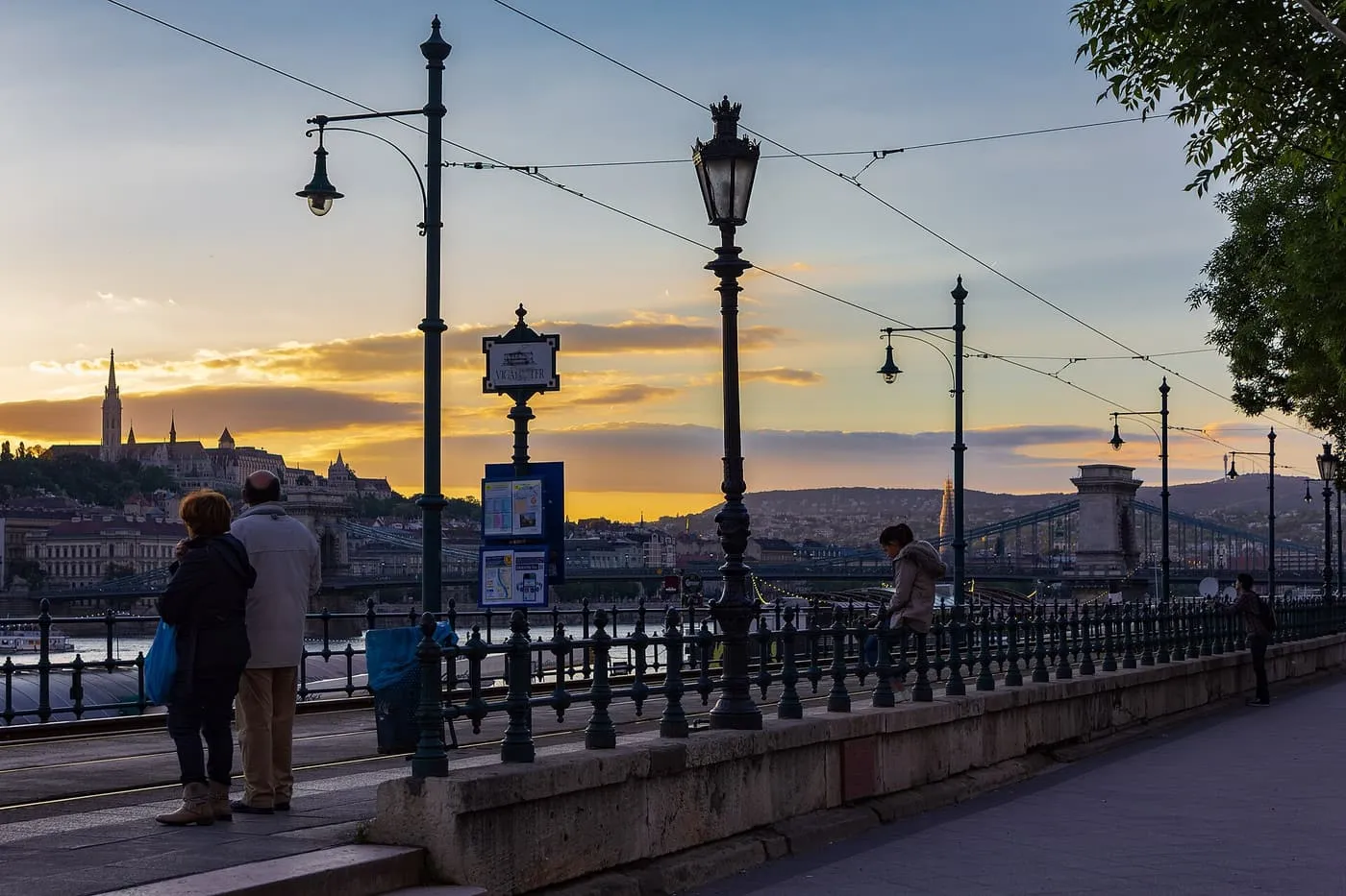 The tram stop at Vigadó tér on the Pest embankment at sunset, with Buda Castle across the Danube