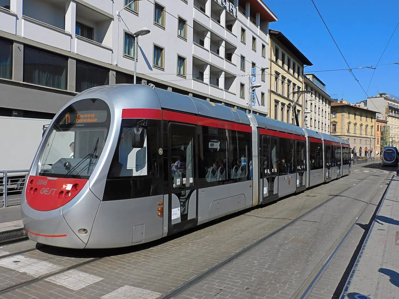 A silver and red tram on Via Alamanni, with tracks set into the street and apartment buildings behind