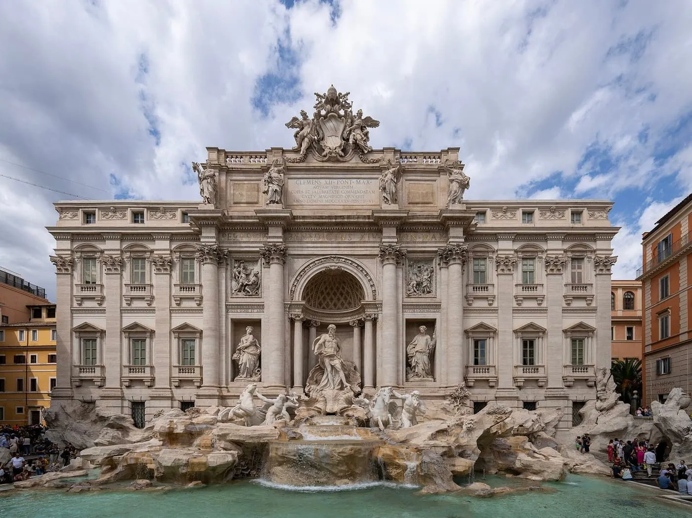 The Trevi Fountain seen across its basin, with visitors on the steps at its right edge