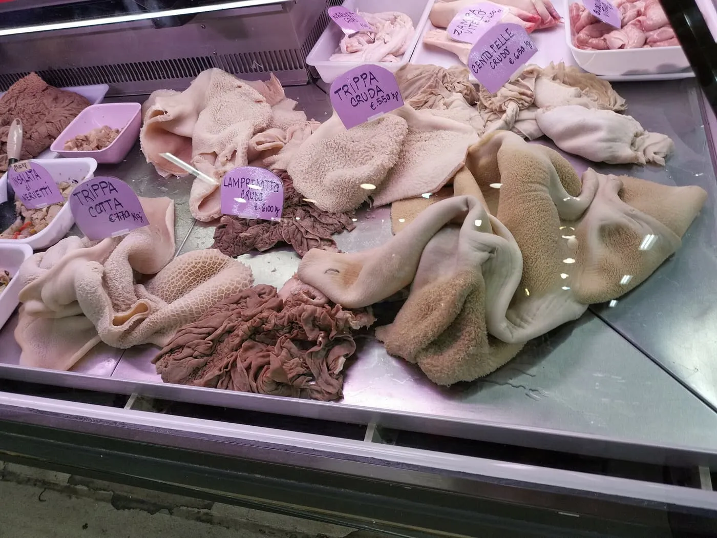 A tripe seller's counter with trays of raw and cooked tripe and lampredotto under purple price labels