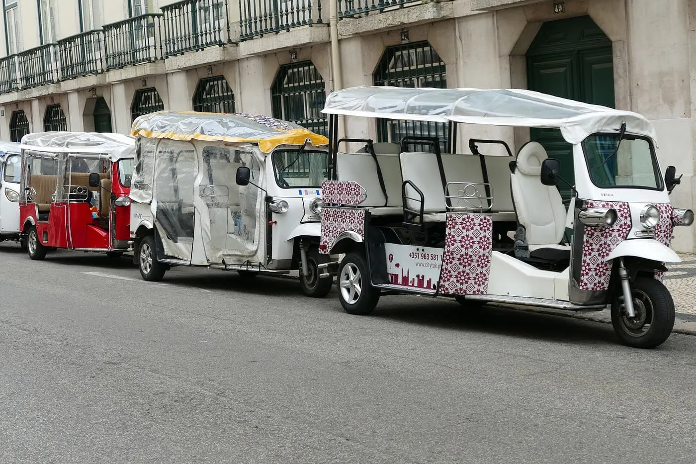 Three tuk-tuks parked in a row along a Lisbon street, one with a tile-pattern panel on its front