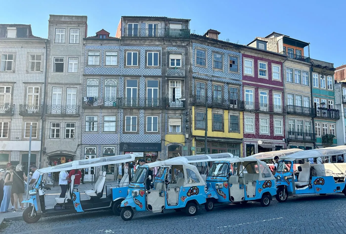 A row of blue tuk-tuks decorated with hearts and flowers, parked on cobbles in front of tiled and painted townhouses