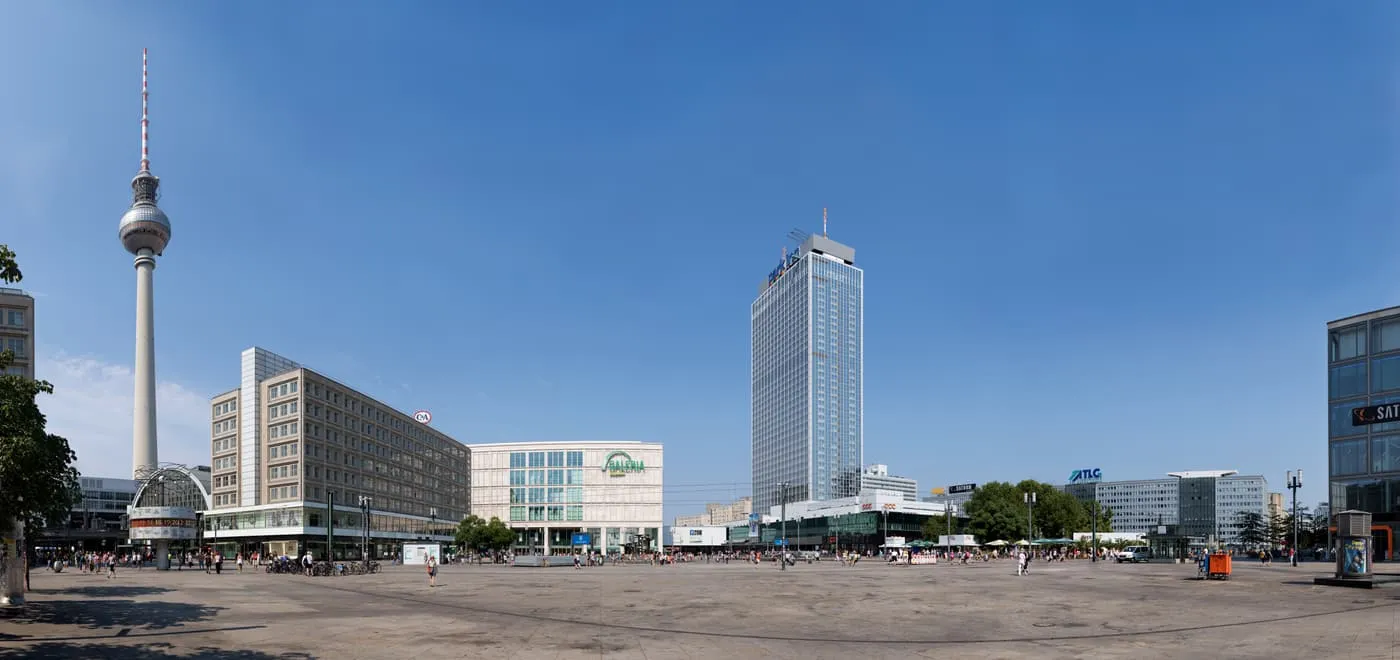 The TV Tower and the buildings around Alexanderplatz under a blue sky, seen across the open square