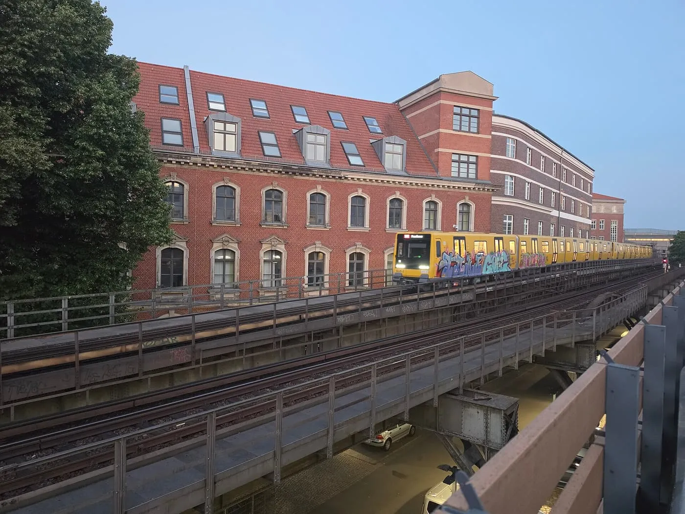A yellow U-Bahn train on the elevated U2 viaduct beside a red-brick building