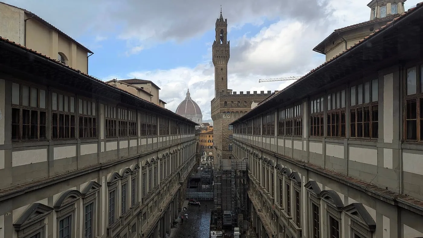 The long arcaded wings of the Uffizi seen from a window, with the Palazzo Vecchio tower and the Duomo dome at the end of the courtyard