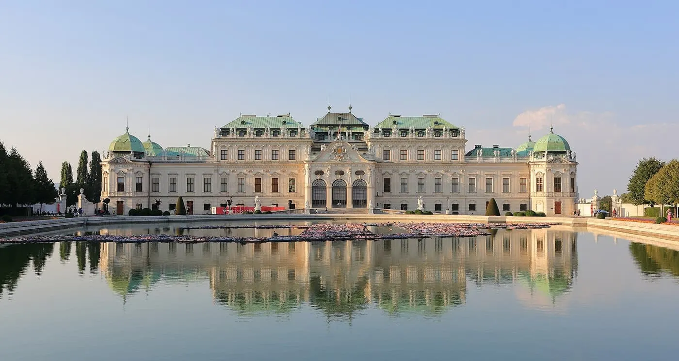 The Upper Belvedere, a long pale baroque palace with green copper roofs, reflected in a pond in its gardens