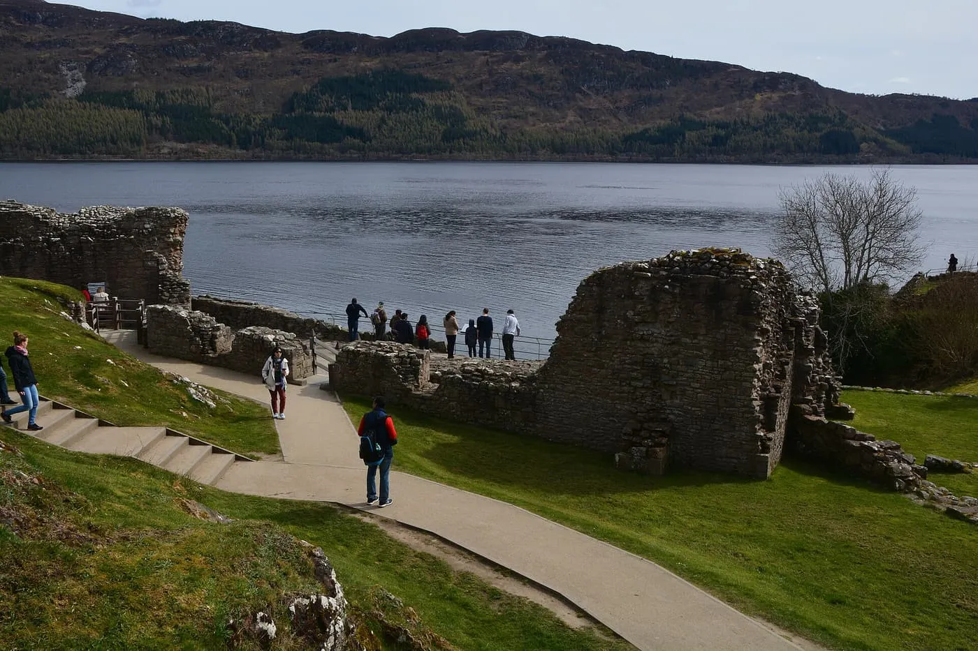 Visitors on a path among the ruined walls of Urquhart Castle, looking out over Loch Ness