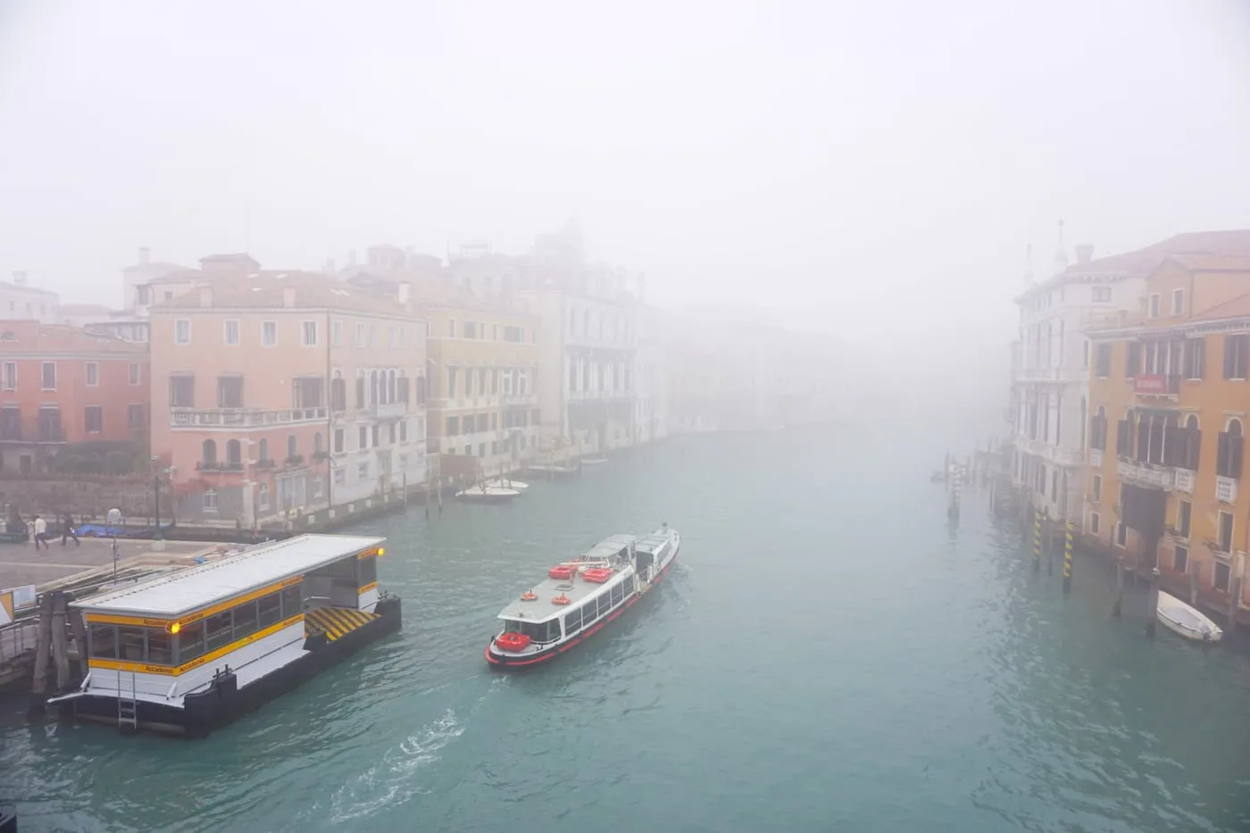 A vaporetto stop and a boat on a wide canal in thick fog, the palaces fading into white