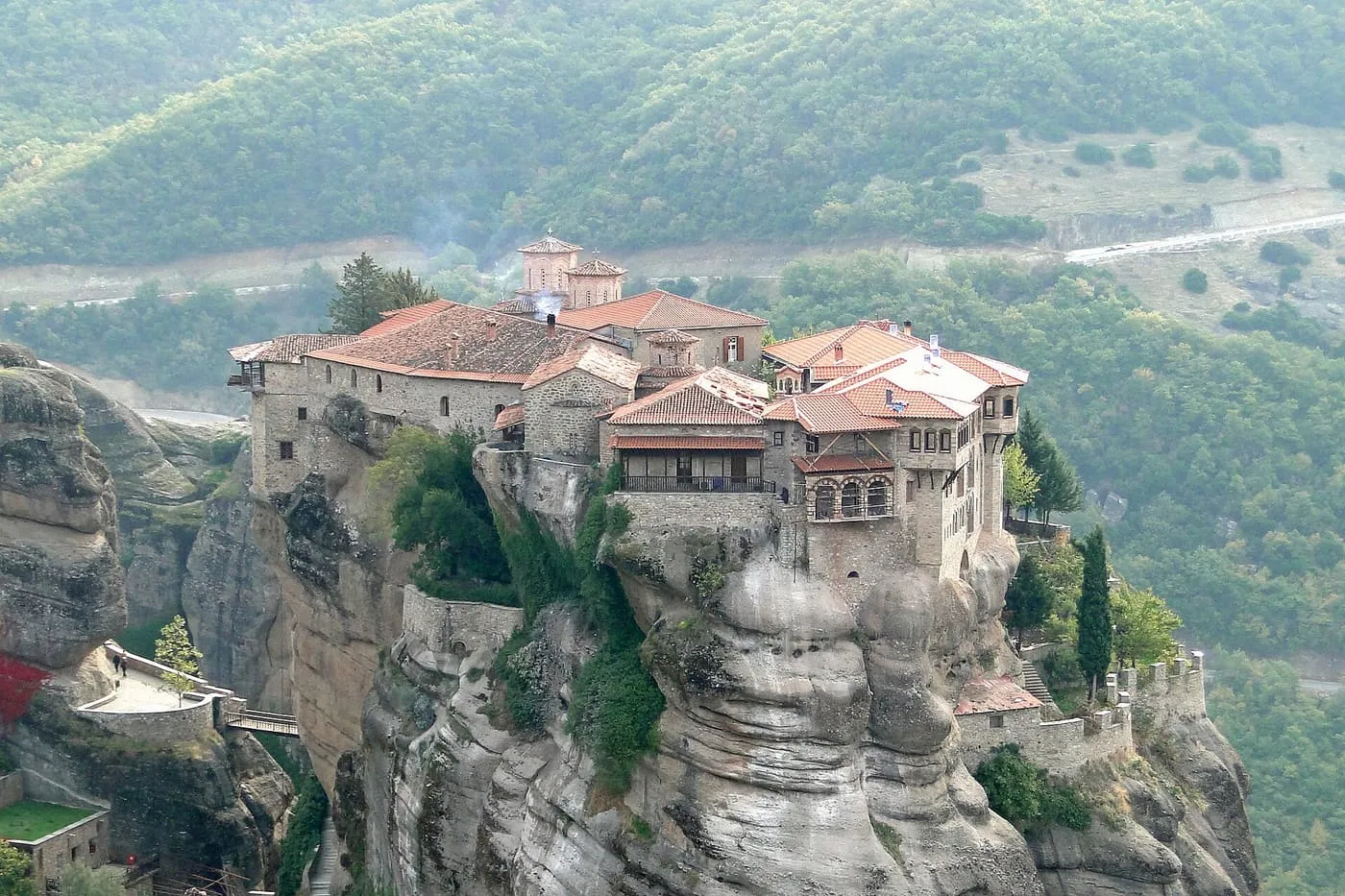 The red-roofed Varlaam monastery crowded onto the top of a narrow rock pillar, with wooded hills behind