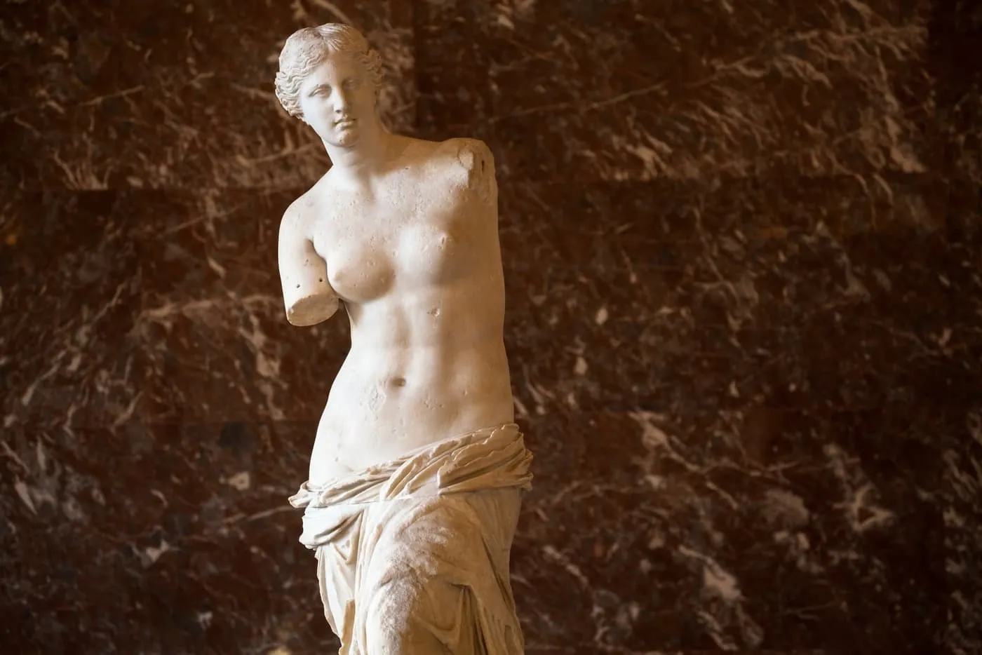 The marble Venus de Milo against a dark red marble wall