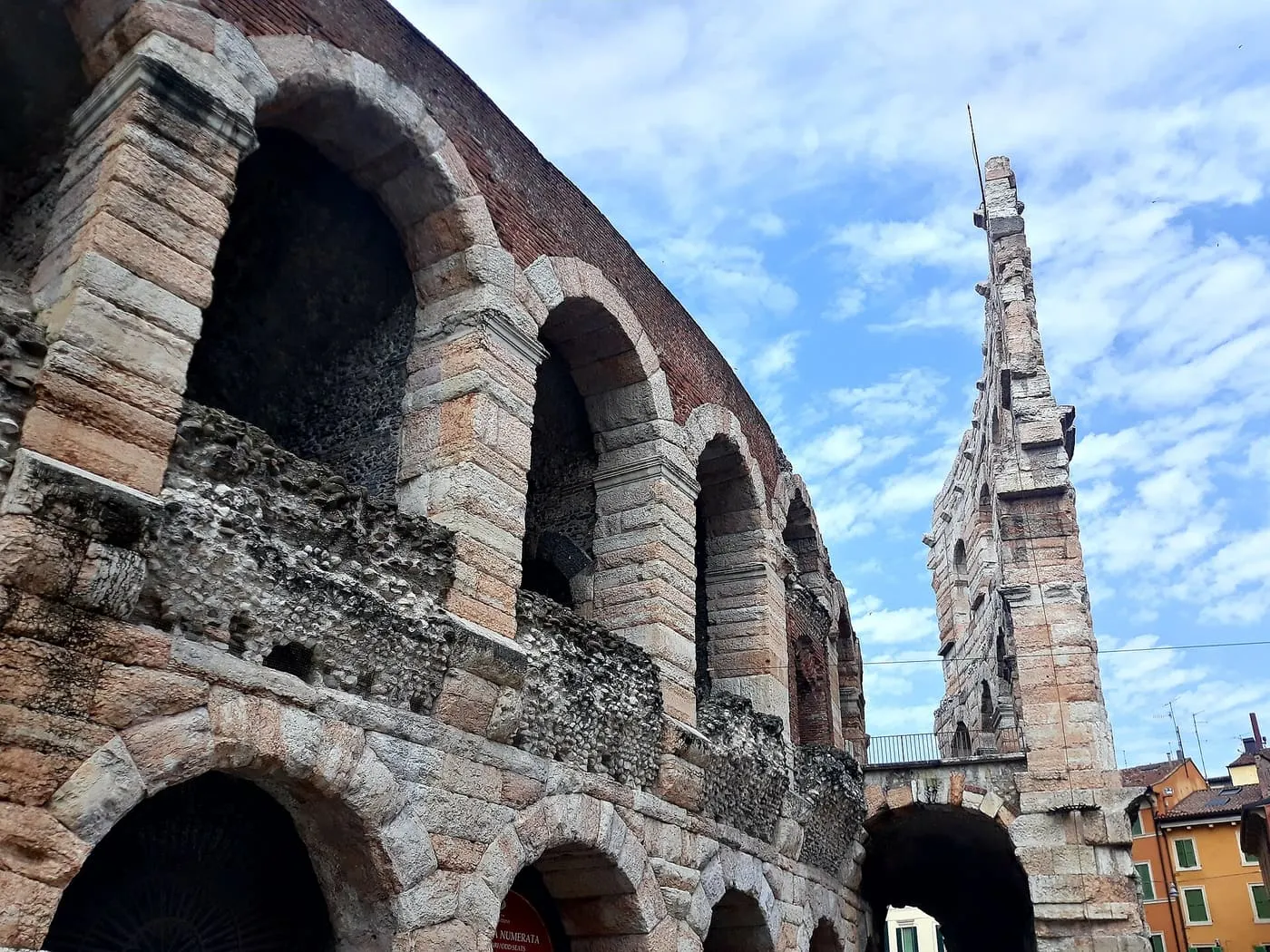 Tall arches of the Verona Arena's surviving outer wall against a blue sky