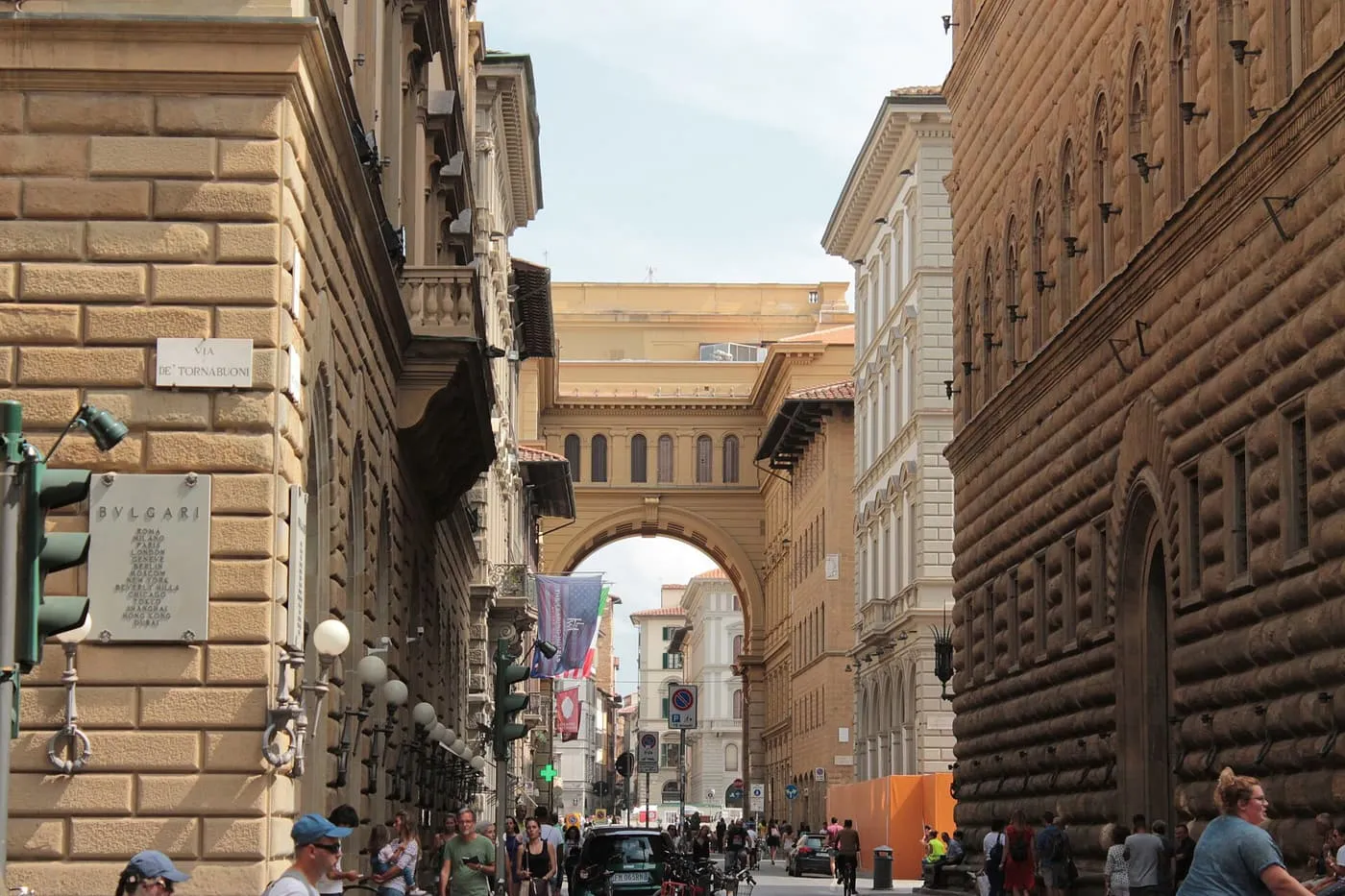 Via de' Tornabuoni running between rusticated stone palaces towards an arch, with pedestrians in the street