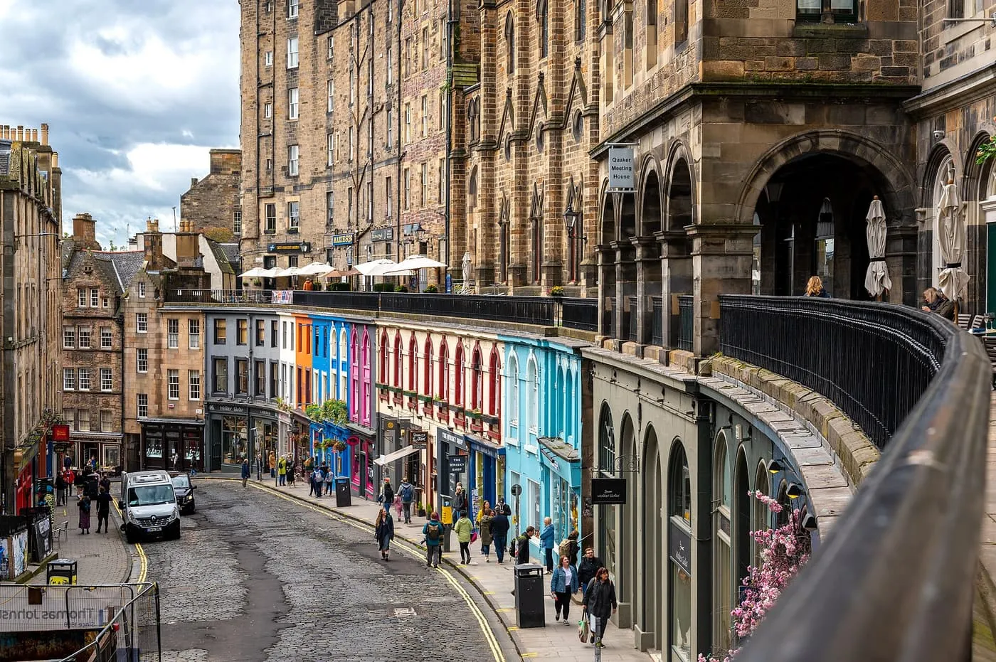 Victoria Street's curved row of painted shopfronts, with a terrace and arcade above and the Old Town tenements behind