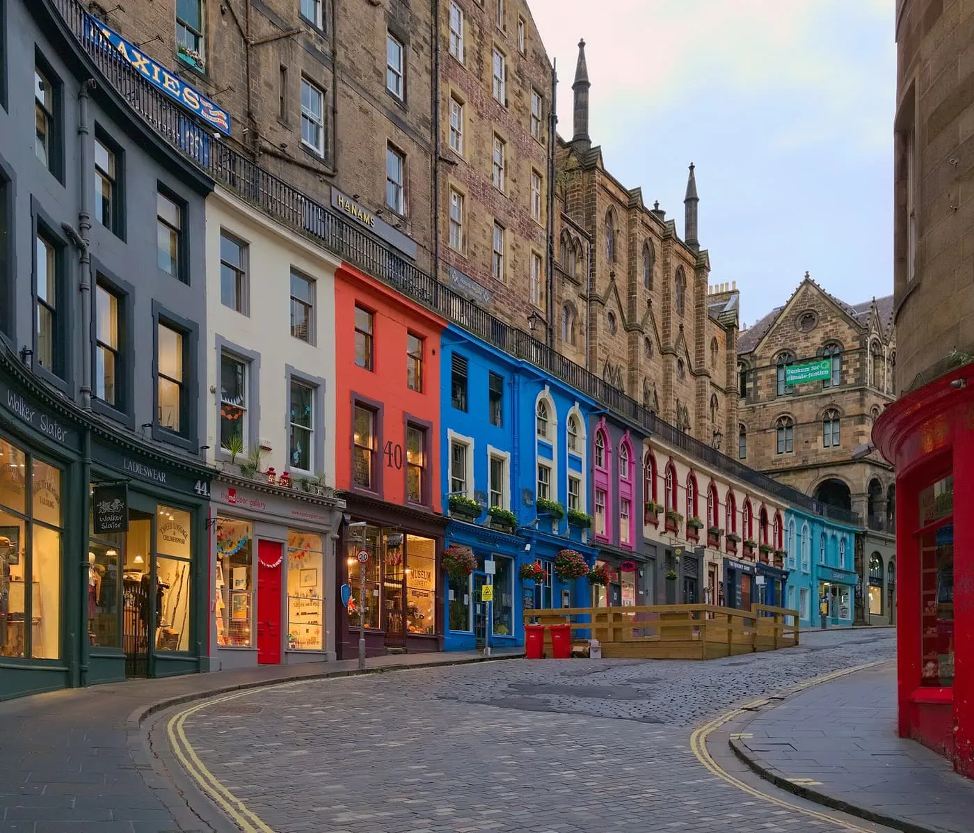 Victoria Street curving up a cobbled slope, its shopfronts painted blue, red, pink and cream under tall stone tenements