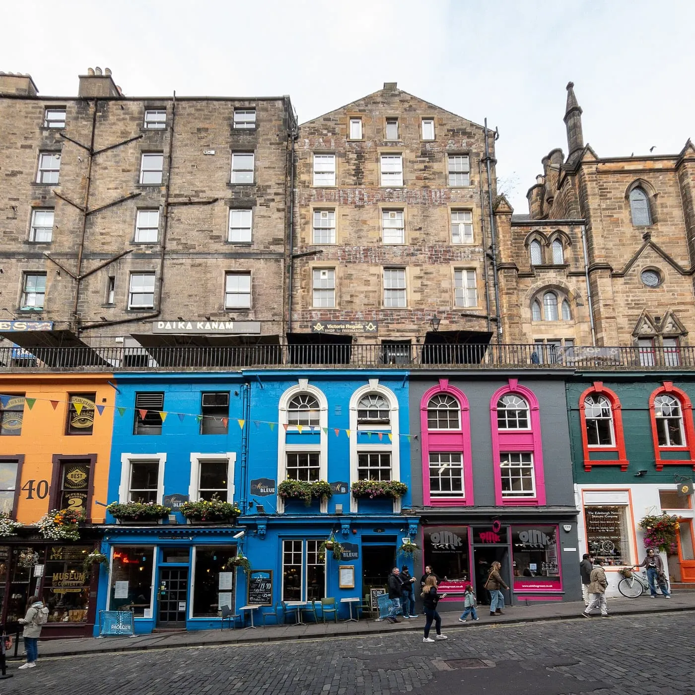 Blue, pink and orange painted shopfronts on Victoria Street, below the stone terrace and tenements