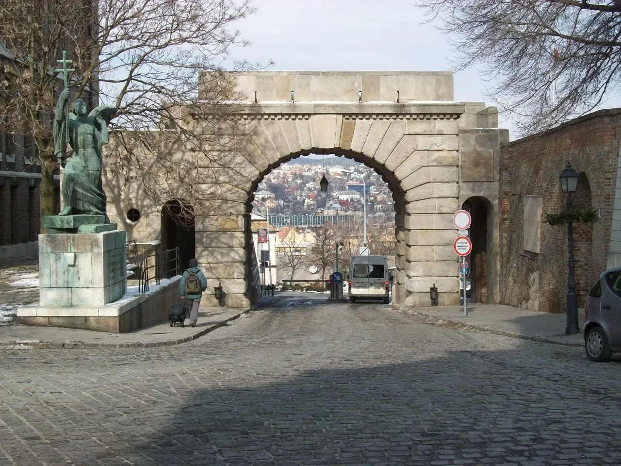 The Vienna Gate, a plain stone arch in the castle wall with a bronze angel statue beside it