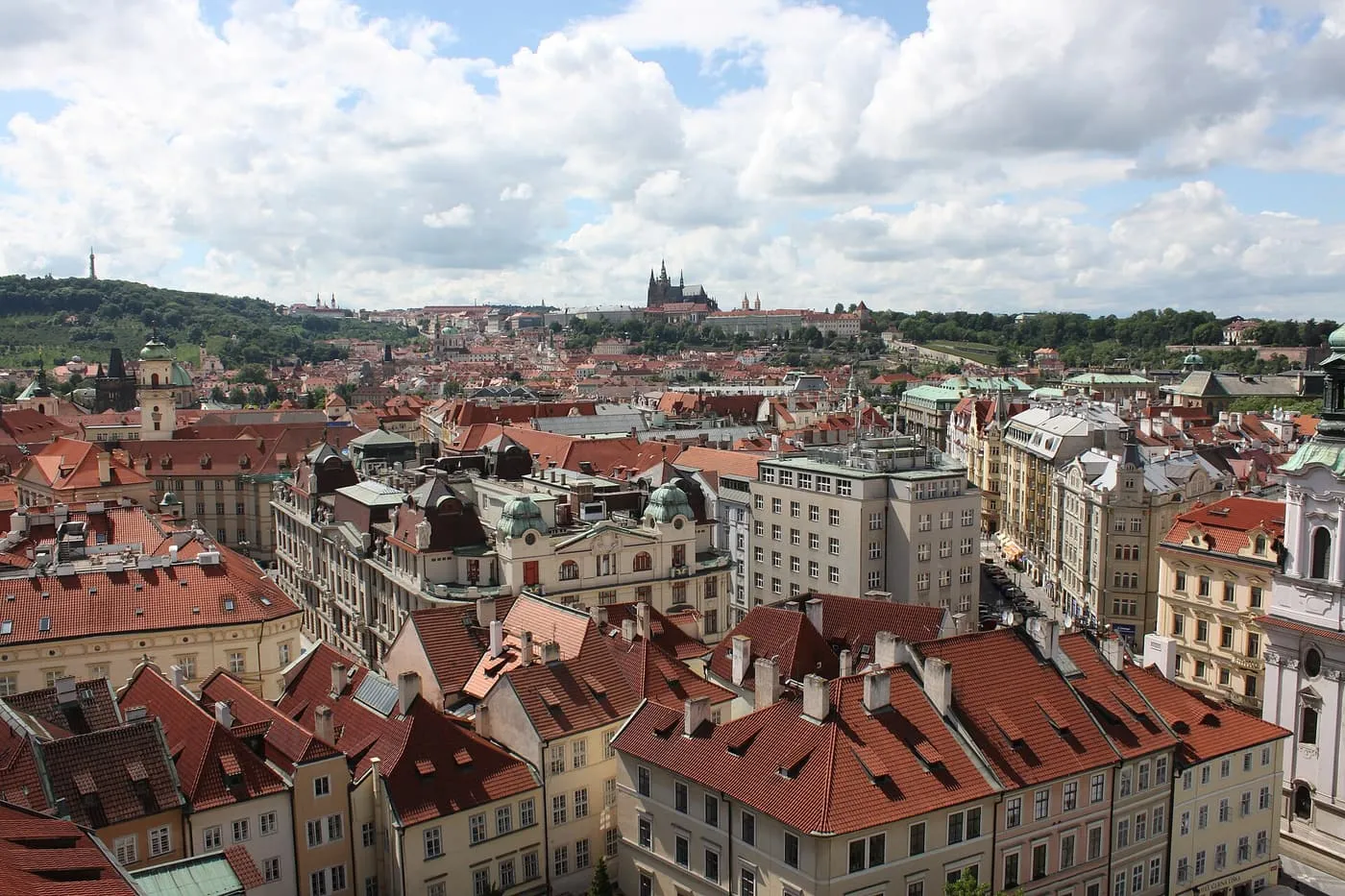 Red-tiled roofs of the Old Town seen from the Old Town Hall tower, with Prague Castle on the hill in the distance