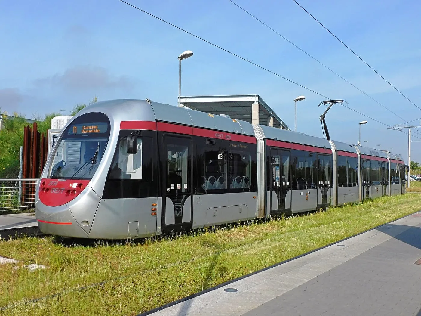 A silver and red T1 tram beside a grass verge at the Villa Costanza terminus in Scandicci