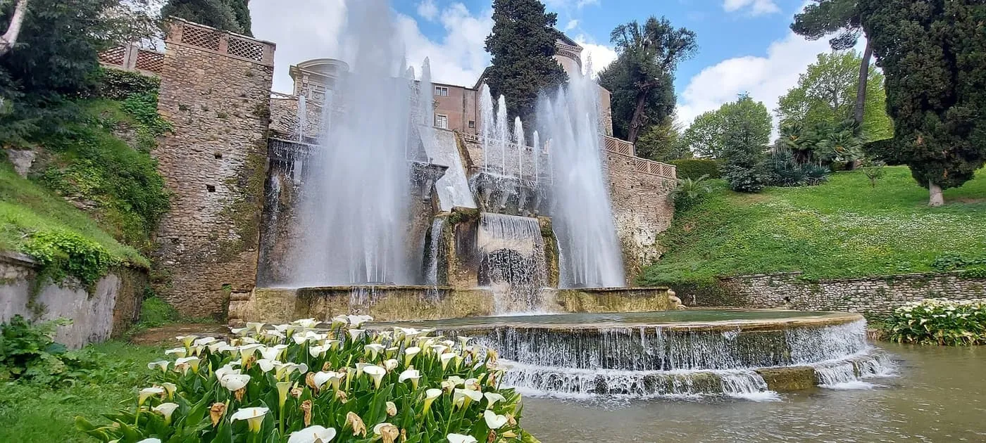 The Organ Fountain at Villa d'Este, with tall jets and a waterfall spilling into a round basin, and white arum lilies in the foreground