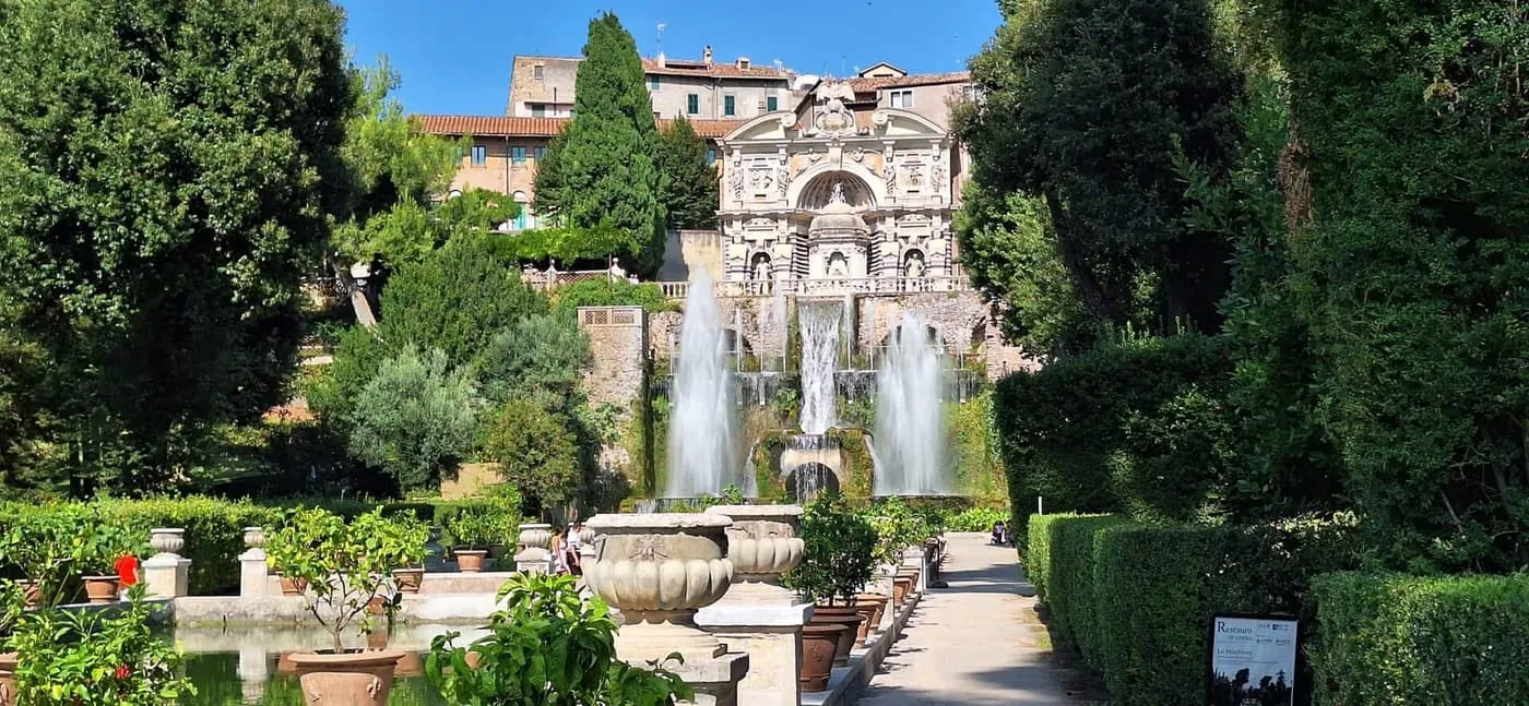 Jets of water in the gardens of Villa d'Este, with a stone building behind the fountains and lemon trees in pots in front