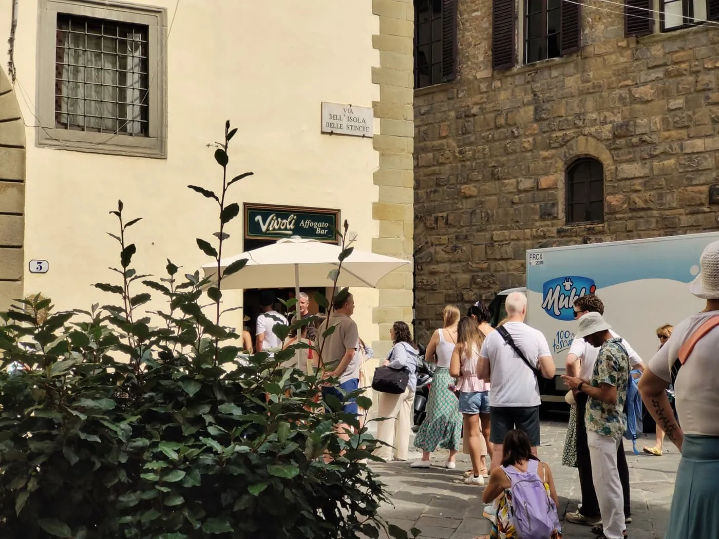 Visitors queuing outside Vivoli on Via dell'Isola delle Stinche, beneath the street sign and a white parasol