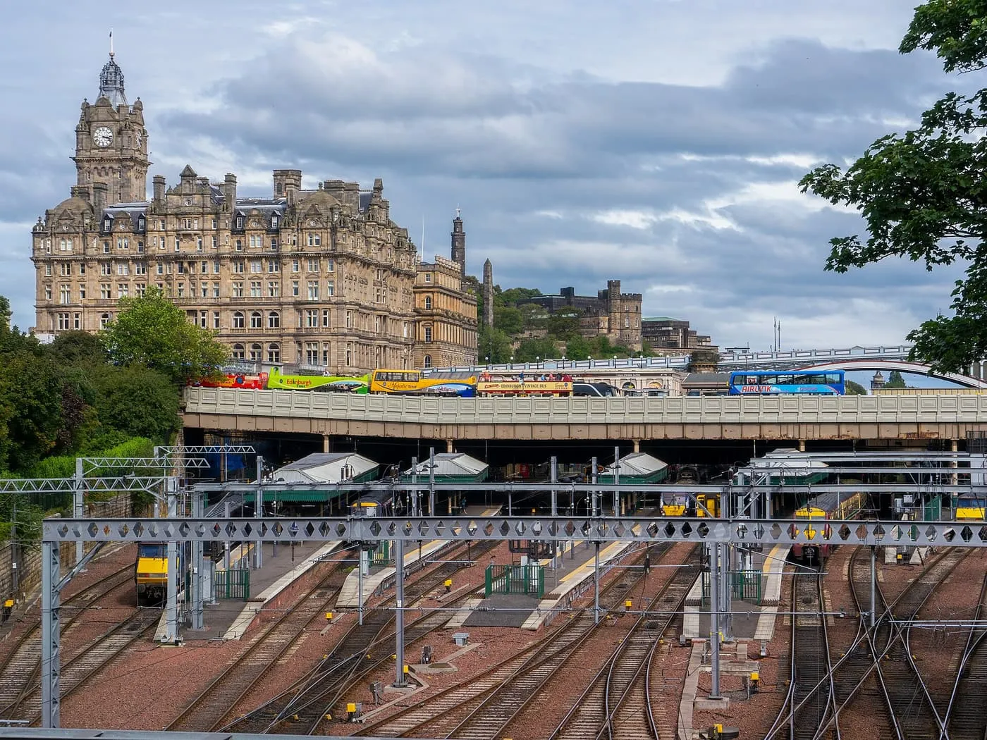 The platforms of Waverley station seen from above, with the Balmoral clock tower and a line of buses on the bridge behind