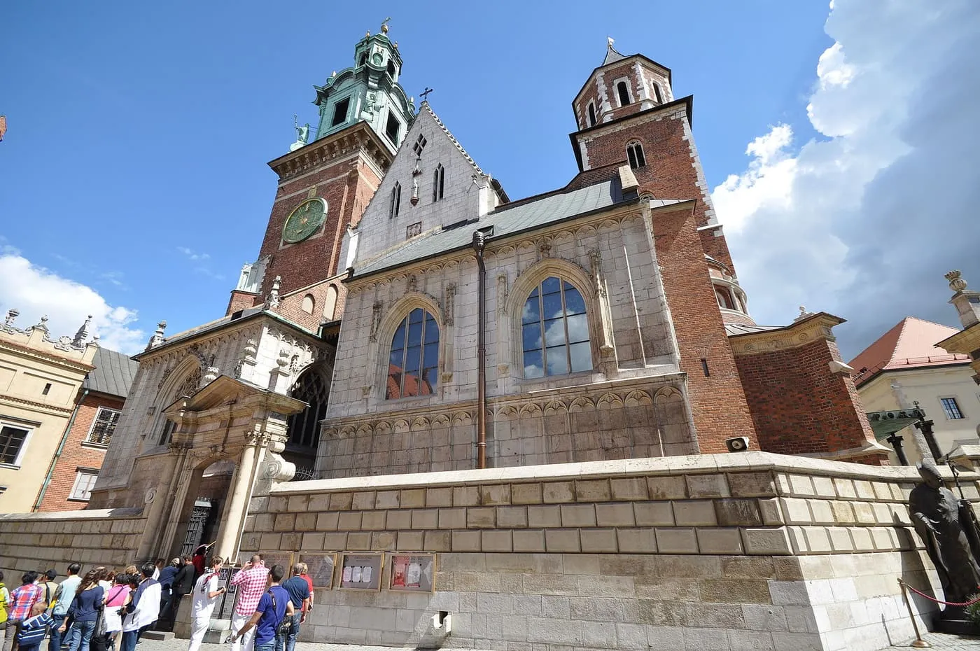 Wawel Cathedral's west front, with its clock tower and a gilded dome, above the steps to the entrance where visitors are gathered