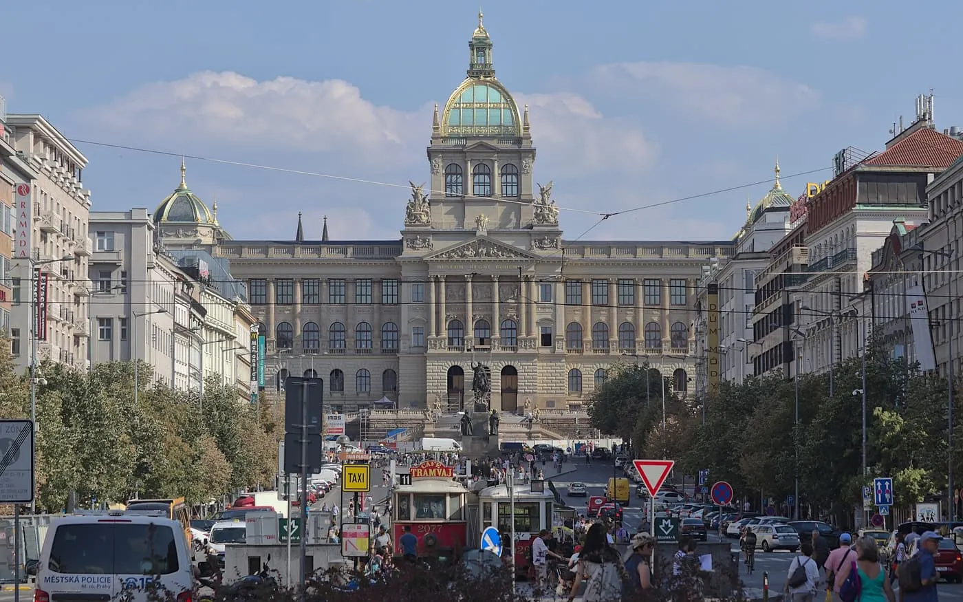 Wenceslas Square in Prague, a wide tree-lined boulevard with a tram and traffic, leading up to the green-domed National Museum