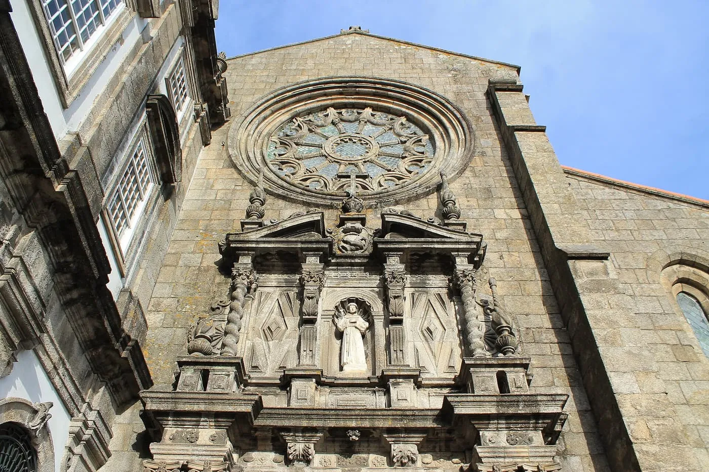 The granite west front of the Igreja de São Francisco, with a Gothic rose window above a Baroque portal and a statue of the saint