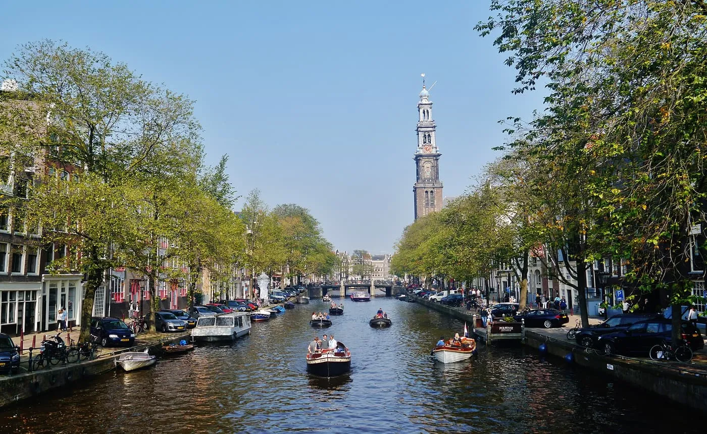 The Westerkerk tower rising above the Prinsengracht, with small boats on the canal and tree-lined quays