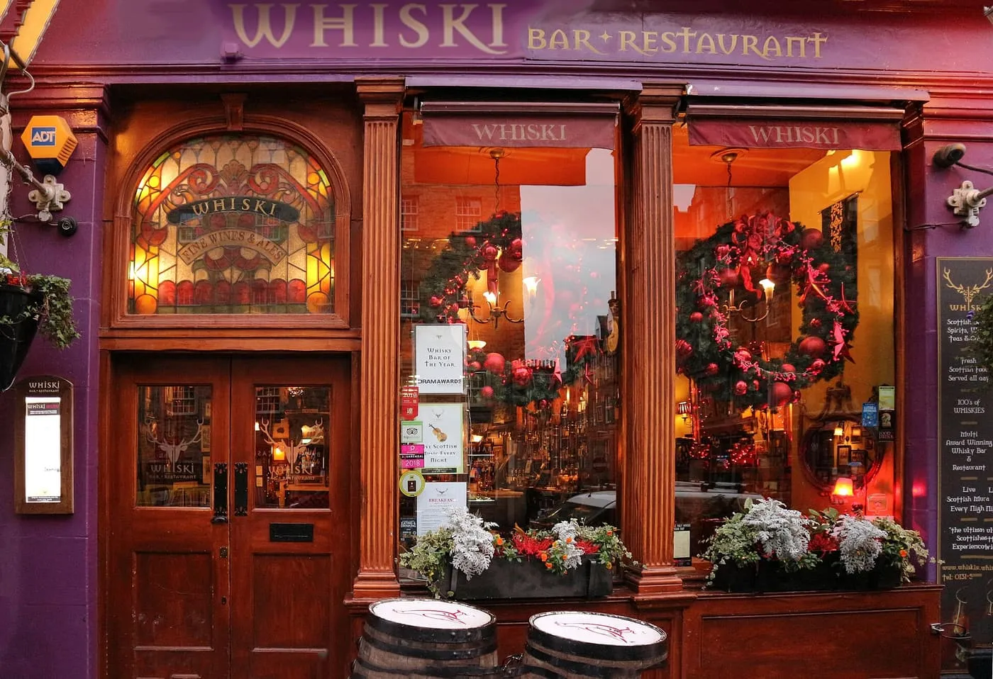 The plum-purple and polished-wood front of Whiski Bar & Restaurant, with a stained-glass fanlight, wreaths in the windows and two whisky barrels by the door