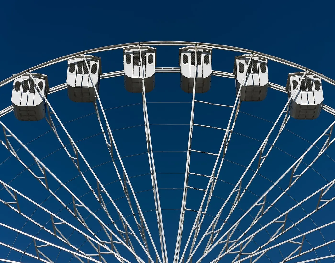 The upper half of a white ferris wheel with its gondolas against a deep blue sky