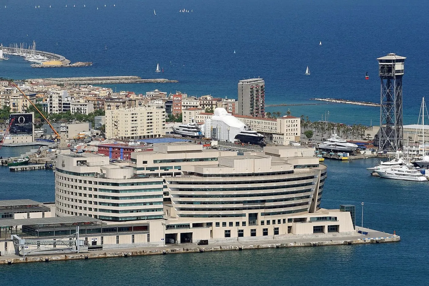 The curved white World Trade Center Barcelona on its pier, seen from above, with the Torre de Jaume I cable-car tower and the harbour beyond